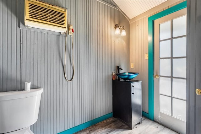 bathroom featuring vanity, lofted ceiling, an AC wall unit, wooden walls, and wood-type flooring