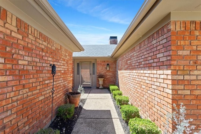 entrance to property with brick siding, a chimney, and a shingled roof