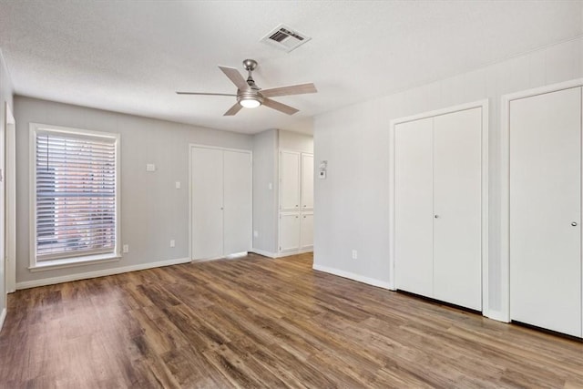 unfurnished bedroom featuring a ceiling fan, wood finished floors, visible vents, baseboards, and two closets