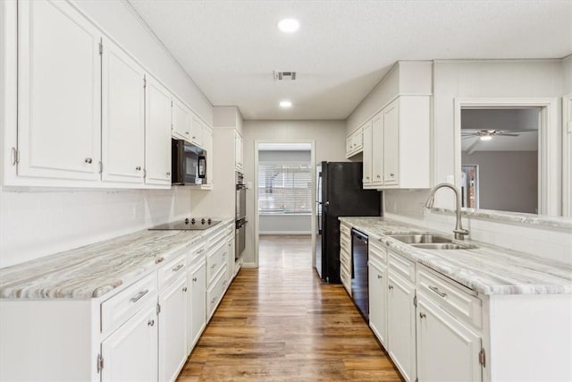 kitchen with white cabinetry, black appliances, light wood-style floors, and a sink