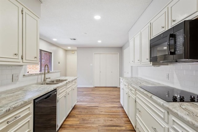 kitchen with white cabinetry, black appliances, light wood-style flooring, and a sink