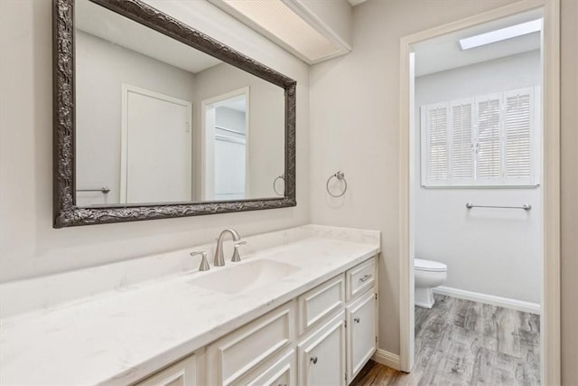 bathroom with vanity, toilet, wood finished floors, and baseboards