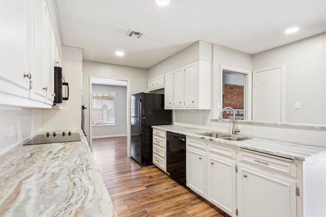 kitchen with white cabinets, black appliances, light wood-type flooring, and a sink