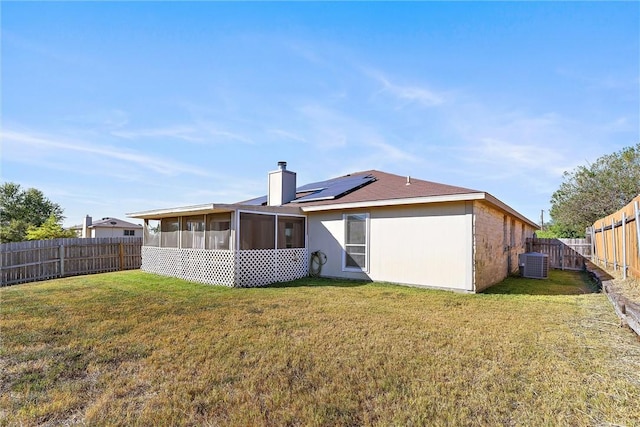 rear view of property with a sunroom, solar panels, a yard, and central AC