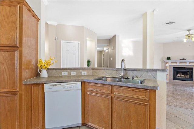 kitchen with white dishwasher, ceiling fan, sink, light tile patterned floors, and a tiled fireplace