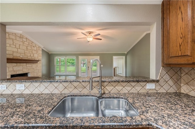 kitchen featuring backsplash, dark stone countertops, crown molding, and sink