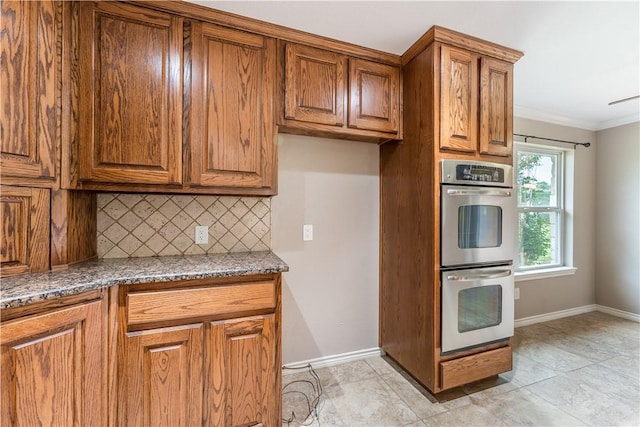 kitchen with stainless steel double oven, tasteful backsplash, dark stone counters, light tile patterned floors, and ornamental molding