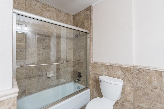 bathroom with toilet, enclosed tub / shower combo, and tile walls