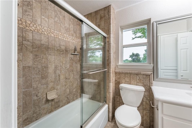 full bathroom featuring a textured ceiling, vanity, shower / bath combination with glass door, tile walls, and toilet