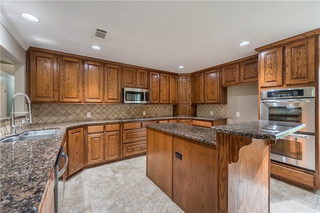 kitchen with sink, stainless steel appliances, dark stone countertops, a breakfast bar area, and a kitchen island