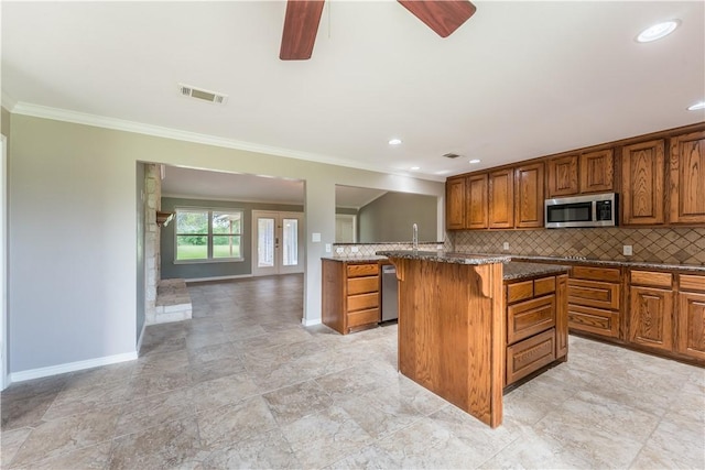 kitchen featuring backsplash, crown molding, appliances with stainless steel finishes, a kitchen island, and a breakfast bar area