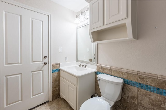 bathroom featuring vanity, toilet, and tile walls