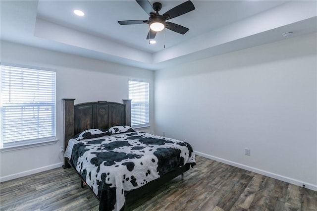 bedroom with a tray ceiling, multiple windows, dark wood-type flooring, and ceiling fan