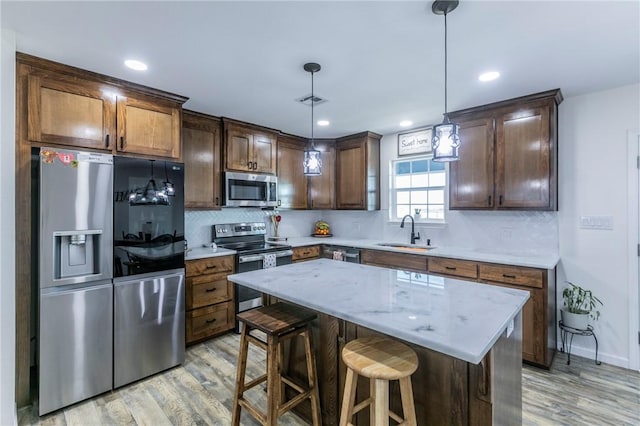 kitchen with light wood-type flooring, stainless steel appliances, sink, pendant lighting, and a kitchen island