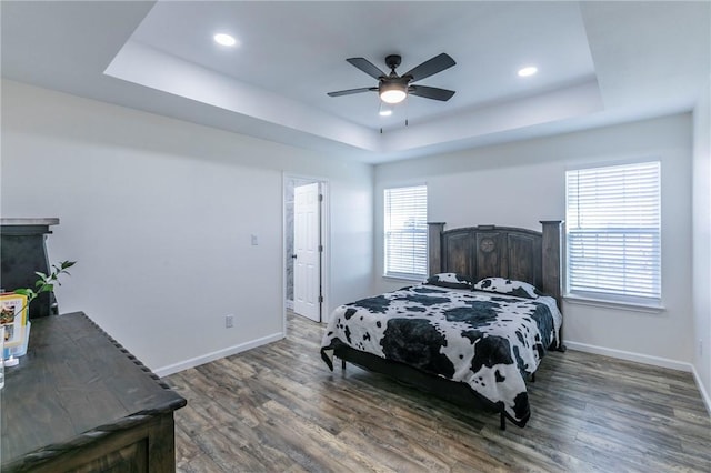 bedroom with dark hardwood / wood-style floors, ceiling fan, and a tray ceiling