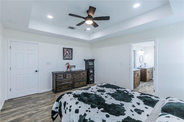 bedroom featuring ensuite bathroom, light hardwood / wood-style flooring, ceiling fan, and a tray ceiling