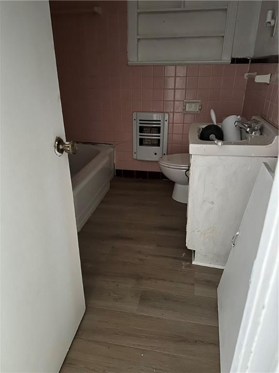 bathroom with a tub, heating unit, toilet, tile walls, and hardwood / wood-style flooring