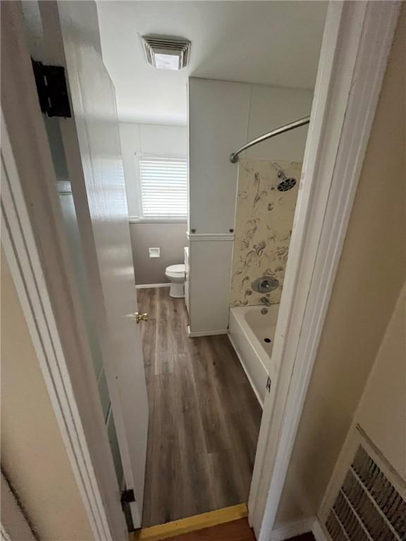 bathroom featuring toilet, wood-type flooring, and shower / washtub combination