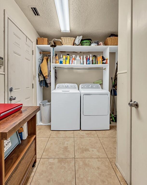 clothes washing area with independent washer and dryer, a textured ceiling, and light tile patterned floors