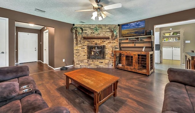 living room featuring a wood stove, ceiling fan, independent washer and dryer, wood-type flooring, and a textured ceiling