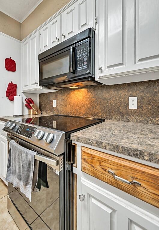 kitchen with electric range, white cabinetry, backsplash, and light tile patterned floors