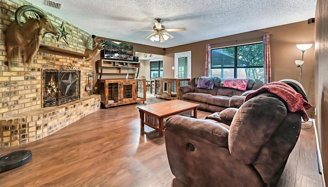 living room with ceiling fan, hardwood / wood-style floors, a textured ceiling, and a brick fireplace