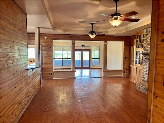 unfurnished living room featuring wooden walls, hardwood / wood-style flooring, ceiling fan, ornate columns, and a tray ceiling