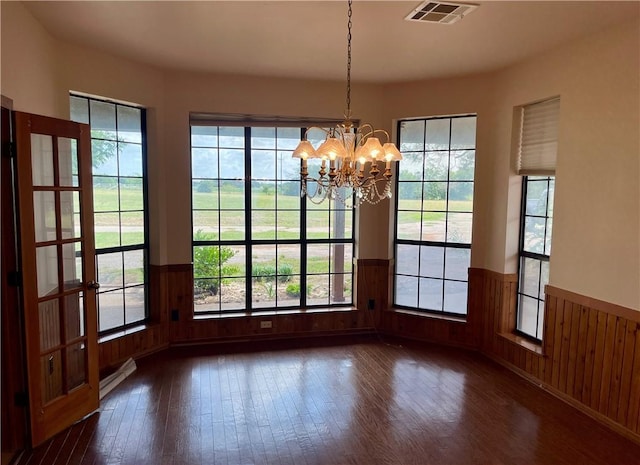 unfurnished dining area featuring a chandelier, wooden walls, and dark wood-type flooring