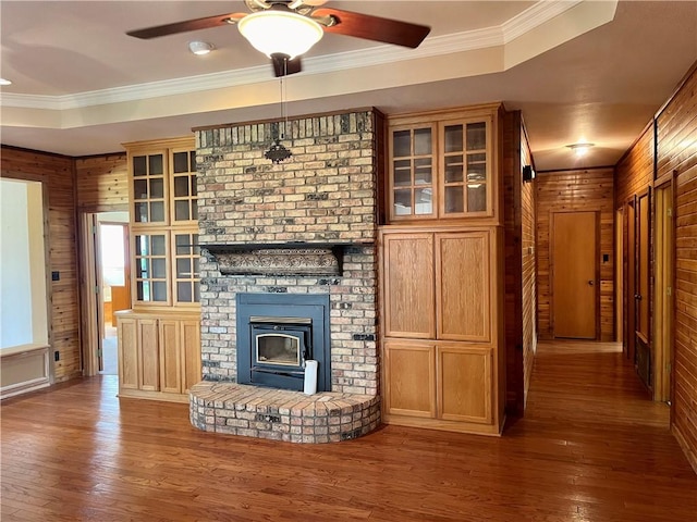 unfurnished living room featuring hardwood / wood-style floors, ceiling fan, wood walls, and ornamental molding