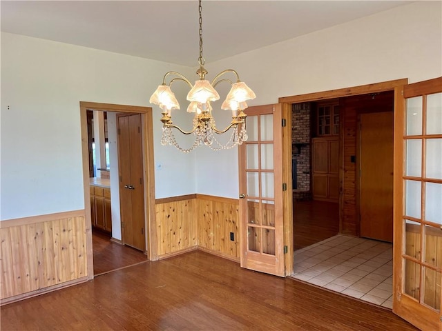 unfurnished dining area with french doors, dark wood-type flooring, wooden walls, and a chandelier