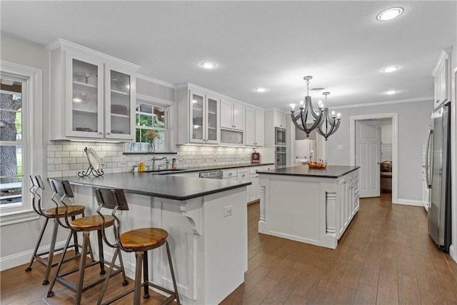 kitchen featuring stainless steel appliances, dark countertops, backsplash, a sink, and a peninsula