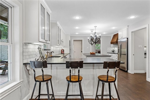 kitchen with dark countertops, a peninsula, stainless steel refrigerator with ice dispenser, and a sink