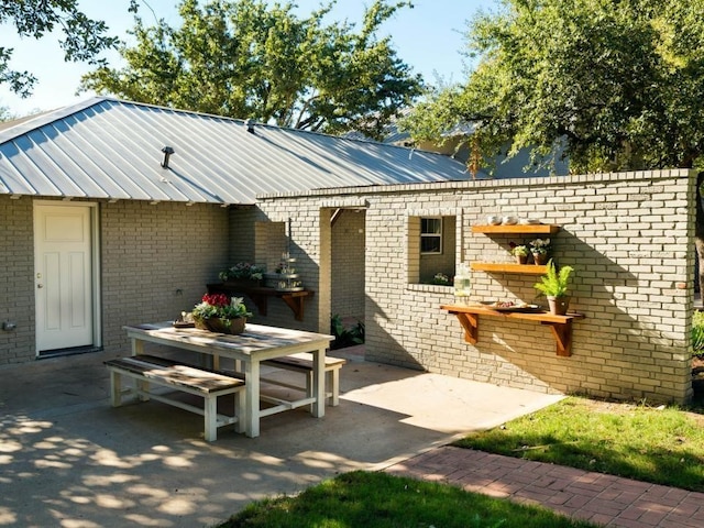 back of house with metal roof, brick siding, and a patio area