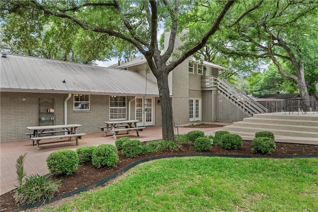 back of house with a patio area, stairway, metal roof, and brick siding