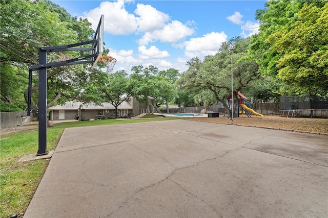 view of basketball court with a trampoline, a playground, basketball hoop, a lawn, and fence