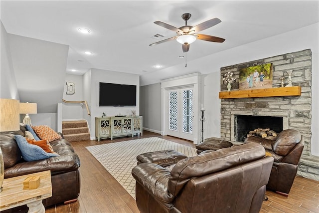 living area featuring a fireplace, wood finished floors, visible vents, a ceiling fan, and stairs