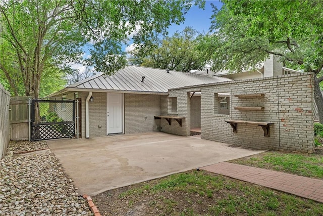 view of front of property with metal roof, a patio, brick siding, fence, and a gate