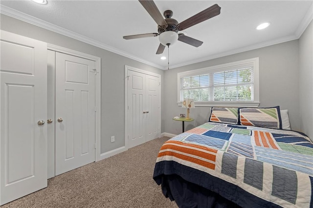 carpeted bedroom featuring ornamental molding, a ceiling fan, baseboards, and two closets