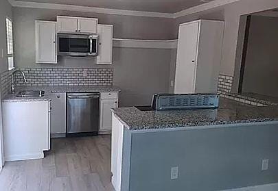 kitchen featuring sink, stainless steel appliances, light stone counters, decorative backsplash, and white cabinets