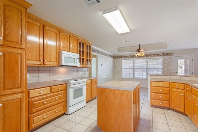 kitchen featuring light countertops, visible vents, glass insert cabinets, a kitchen island, and white appliances