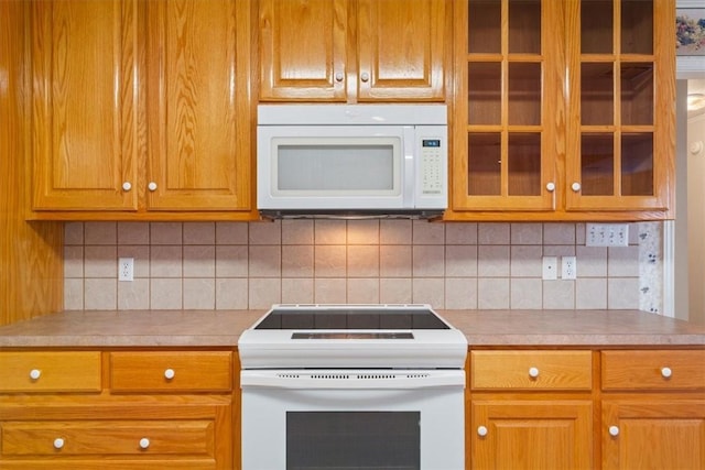 kitchen featuring brown cabinets, white appliances, glass insert cabinets, and light countertops