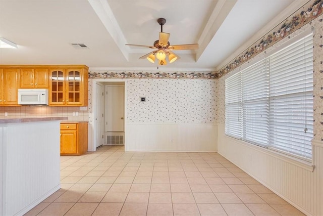 kitchen with a raised ceiling, light countertops, visible vents, white microwave, and glass insert cabinets