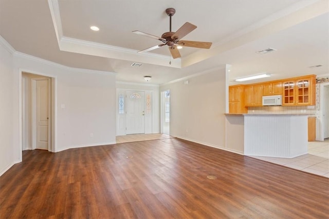 unfurnished living room with visible vents, ornamental molding, a raised ceiling, and wood finished floors