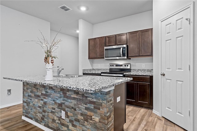 kitchen with appliances with stainless steel finishes, light wood-type flooring, a center island with sink, and sink