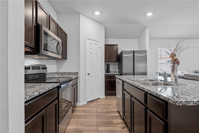 kitchen with appliances with stainless steel finishes, dark brown cabinets, sink, a center island with sink, and light hardwood / wood-style flooring