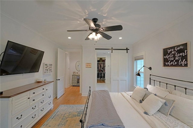 bedroom with ceiling fan, a barn door, ornamental molding, and light hardwood / wood-style floors