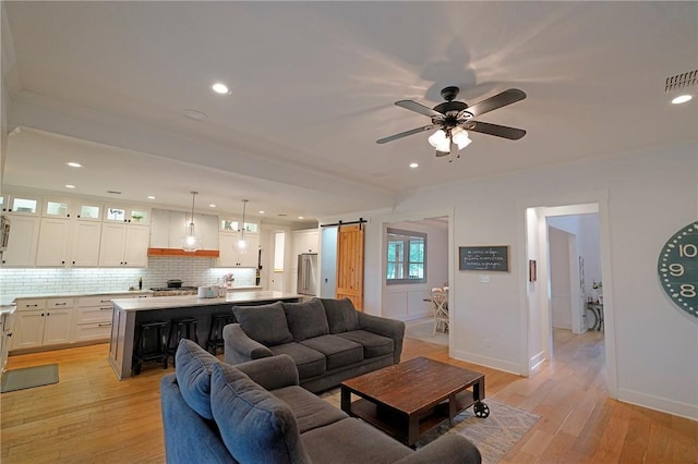 living room with light hardwood / wood-style floors, ceiling fan, crown molding, and a barn door