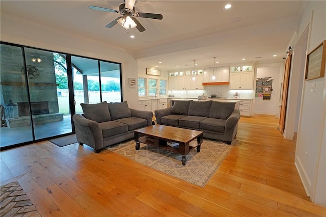 living room with light wood-type flooring, ceiling fan, crown molding, and sink