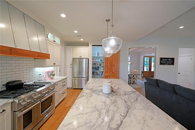 kitchen with pendant lighting, white cabinets, light stone countertops, decorative backsplash, and stainless steel appliances