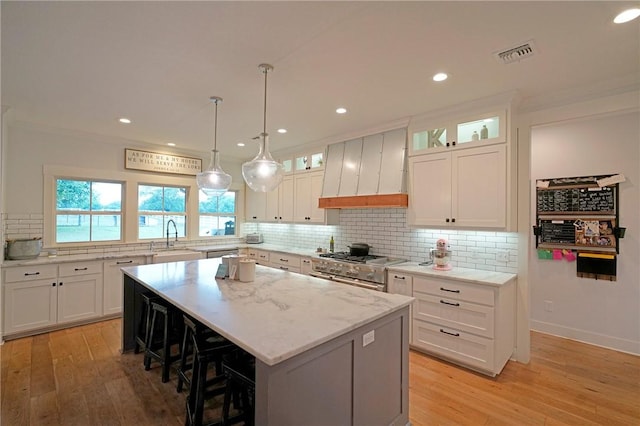 kitchen featuring premium range hood, a center island, white cabinets, and light stone countertops